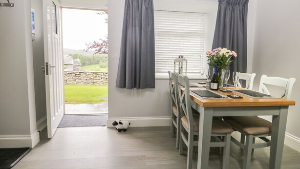 Un comedor con una mesa dispuesta para dos, una ventana con cortinas, una puerta que da al exterior y una pequeña planta de interior.