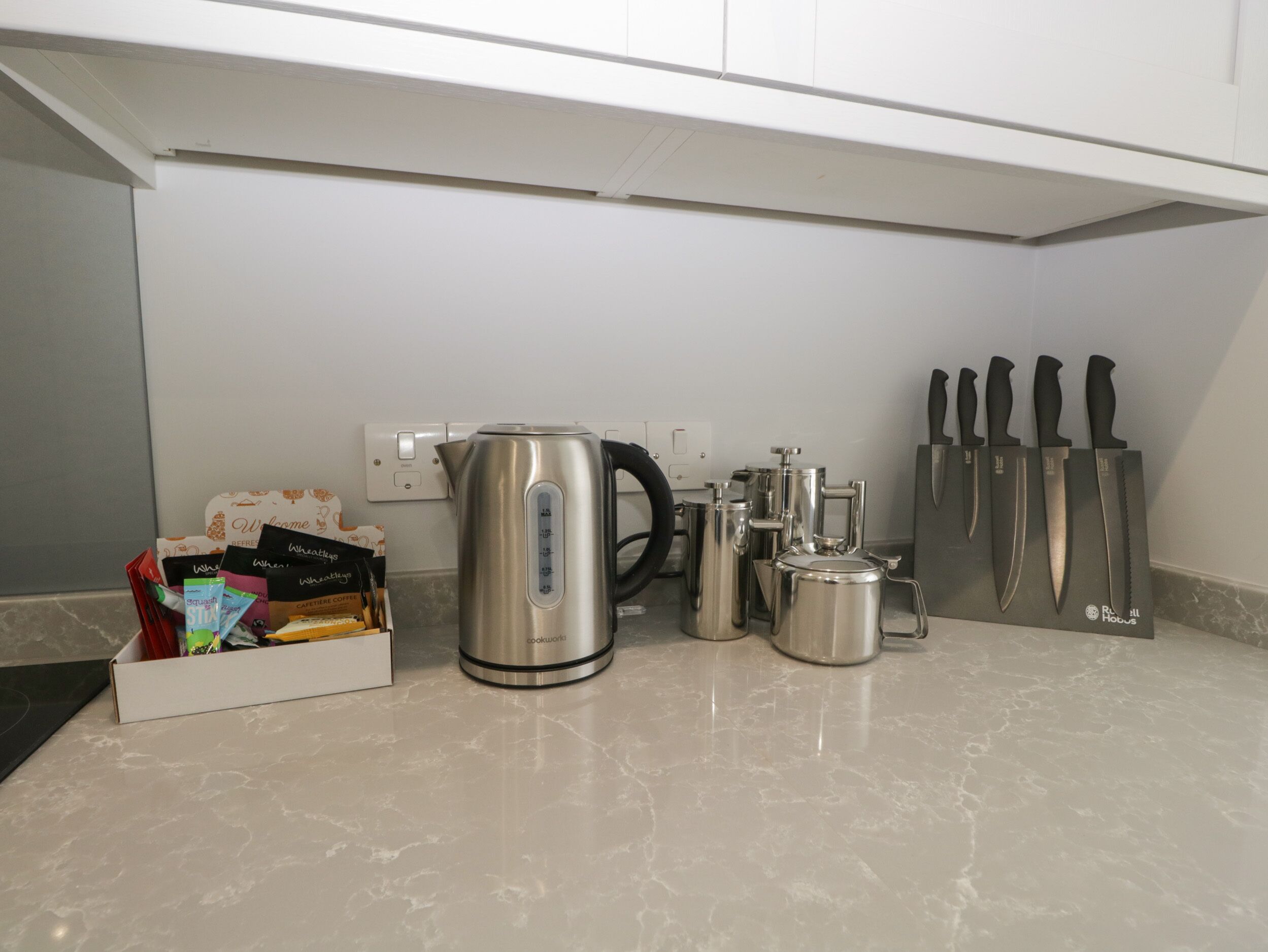 A kitchen with a kettle, coffee maker, and knives on the counter.