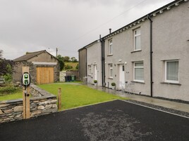 Una calle residencial con una estación de carga para vehículo eléctrico, muros de piedra y un área con césped.