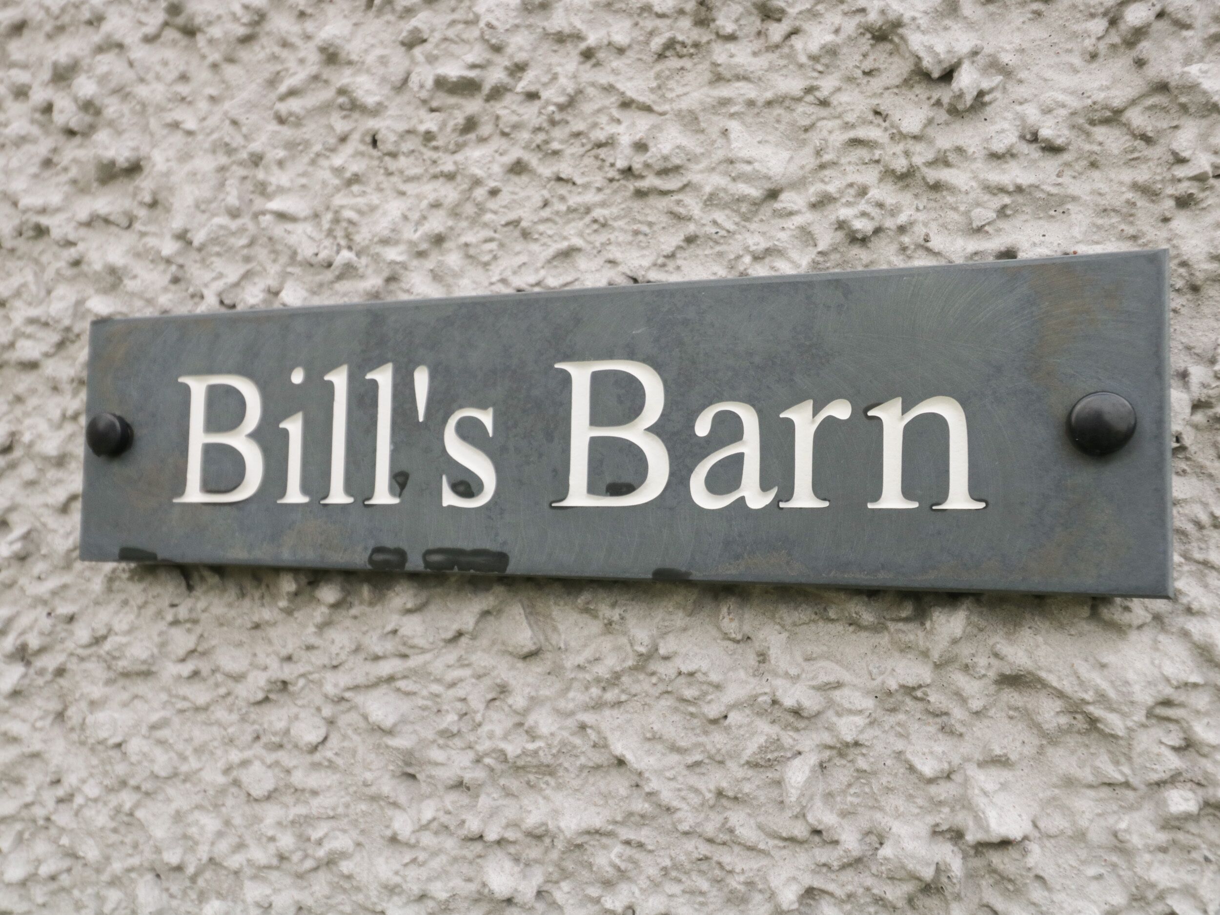Un letrero de metal con el texto 'Bill's Barn' sujeto a una pared con textura.