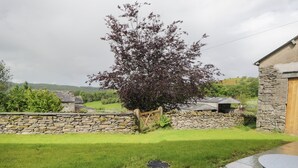 Un muro de piedra, un césped verde y un árbol con hojas moradas.