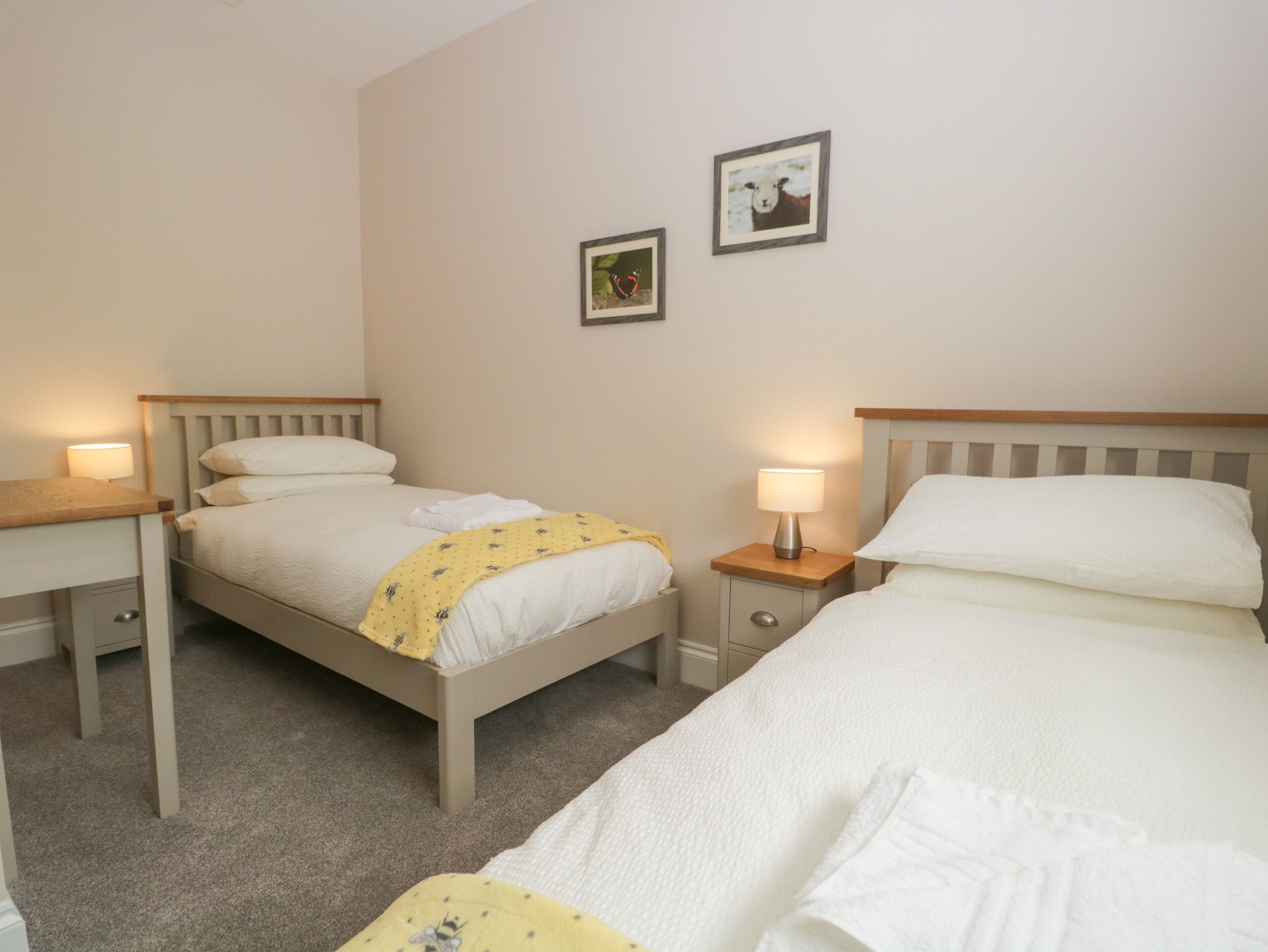 A hotel room with two single beds, a desk, and a nightstand with lamps.