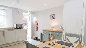 A modern kitchen with white cabinets, a microwave, and a dining area with a wooden table set for two. - Oxen Park Farm Cottage (Ulverston)