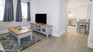 A modern living room with a flat-screen TV, a wooden coffee table, and a grey rug. - Oxen Park Farm Cottage (Ulverston)