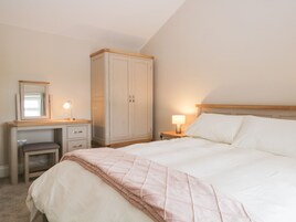 A bedroom with a bed, a desk, a chair, a wardrobe, and a nightstand with a lamp.