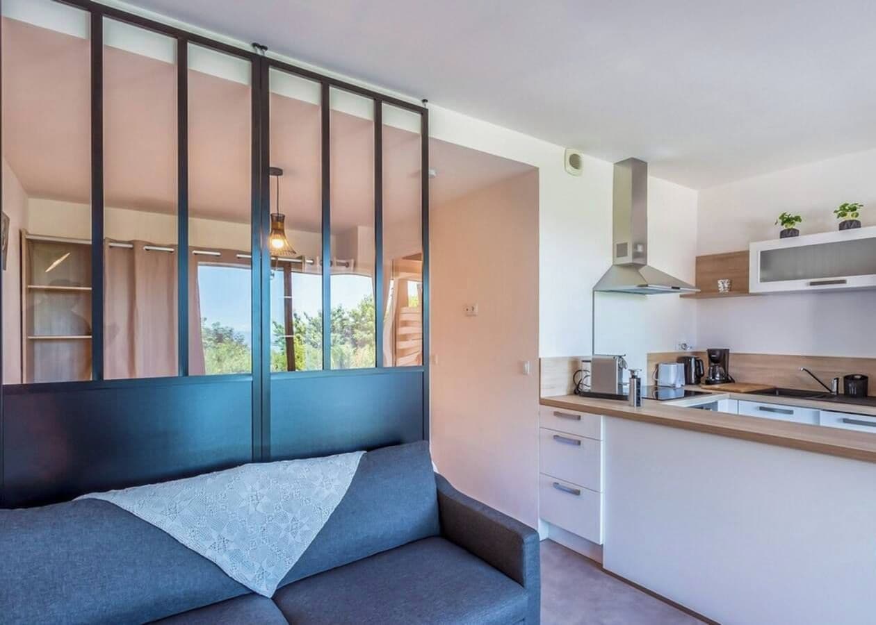 A modern kitchen with a built-in island, white cabinets, and a view through a large window.