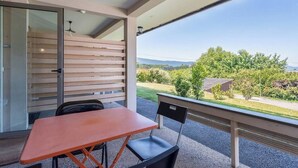 Varanda com mesa e cadeiras, porta de vidro deslizante e vista para um jardim e colinas ao longe.