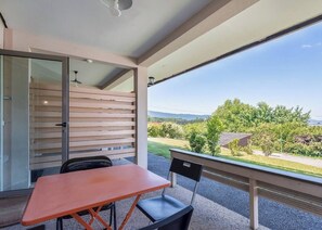 Un balcon avec une table et des chaises, une porte-fenêtre coulissante et une vue sur un jardin et des collines lointaines.