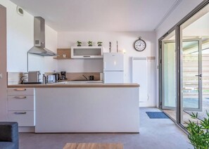 Une cuisine moderne dotée d’un îlot central, d’appareils électroménagers intégrés et d’une grande fenêtre qui laisse entrer la lumière naturelle.