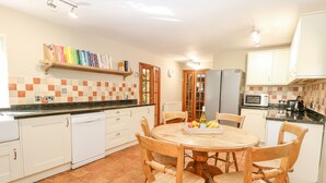 Eine Küche mit weißen Schränken, einer gefliesten Spritzschutzleiste, einem Holztisch mit Stühlen, einer Mikrowelle und einem Kühlschrank.