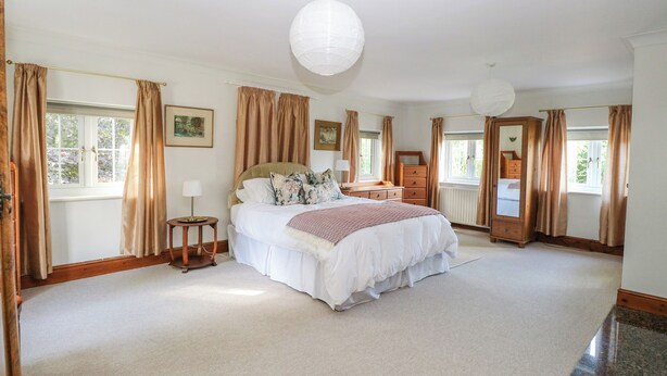 A spacious bedroom with a large bed, a wooden wardrobe, a bedside table, and a large window with curtains.
