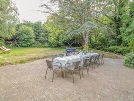 Un área de comedor al aire libre con una mesa dispuesta para seis personas, rodeada de sillas de mimbre, en un exuberante jardín.