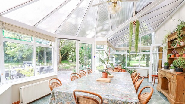 Ein Wintergarten mit Esstisch, Stühlen und Blumentöpfen.