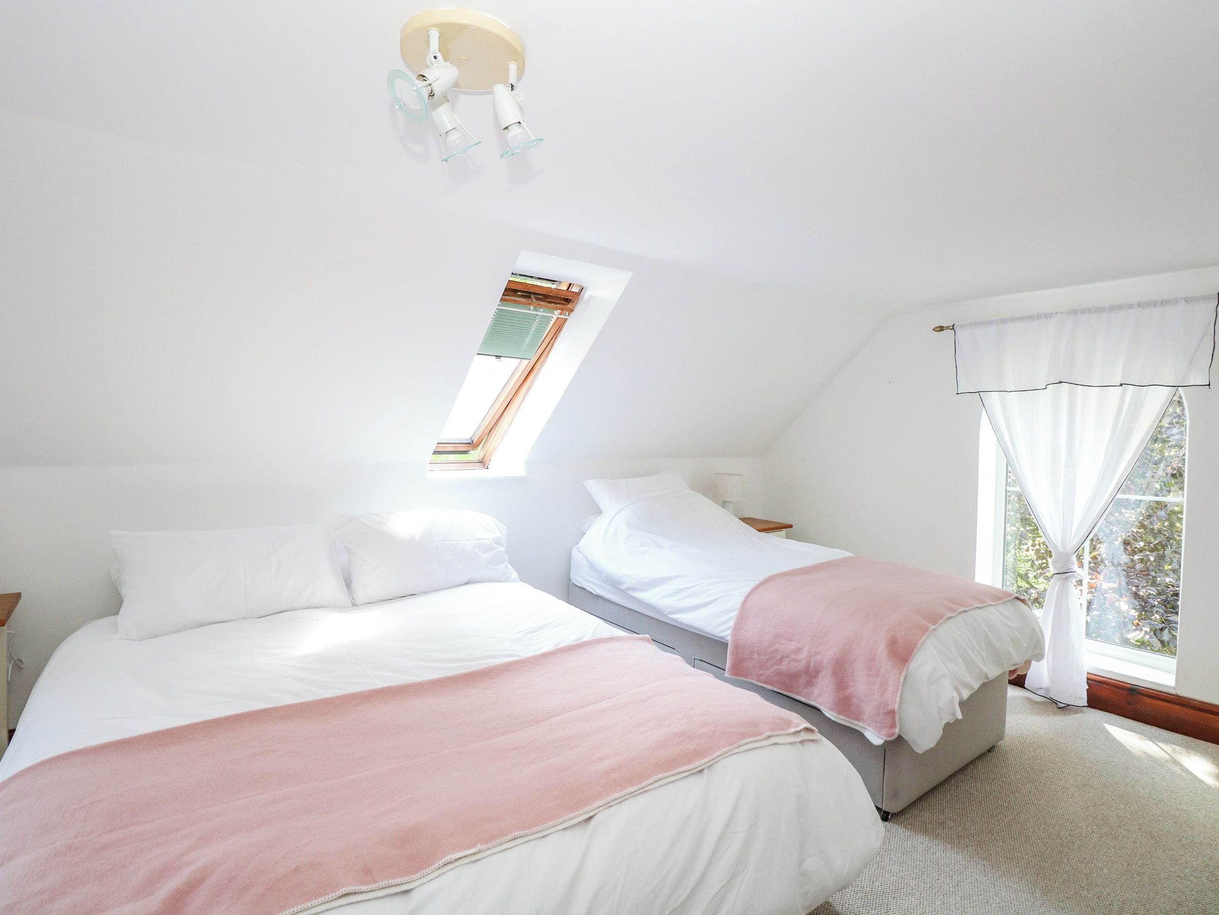 Une chambre avec deux lits, un puits de lumière, une fenêtre avec des rideaux et une table de chevet.
