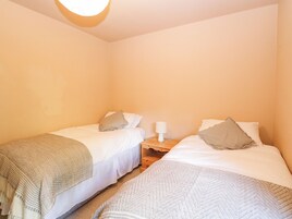 Una habitación con dos camas individuales, cada una con almohada y manta. Hay una mesita de noche con lámpara entre las camas.