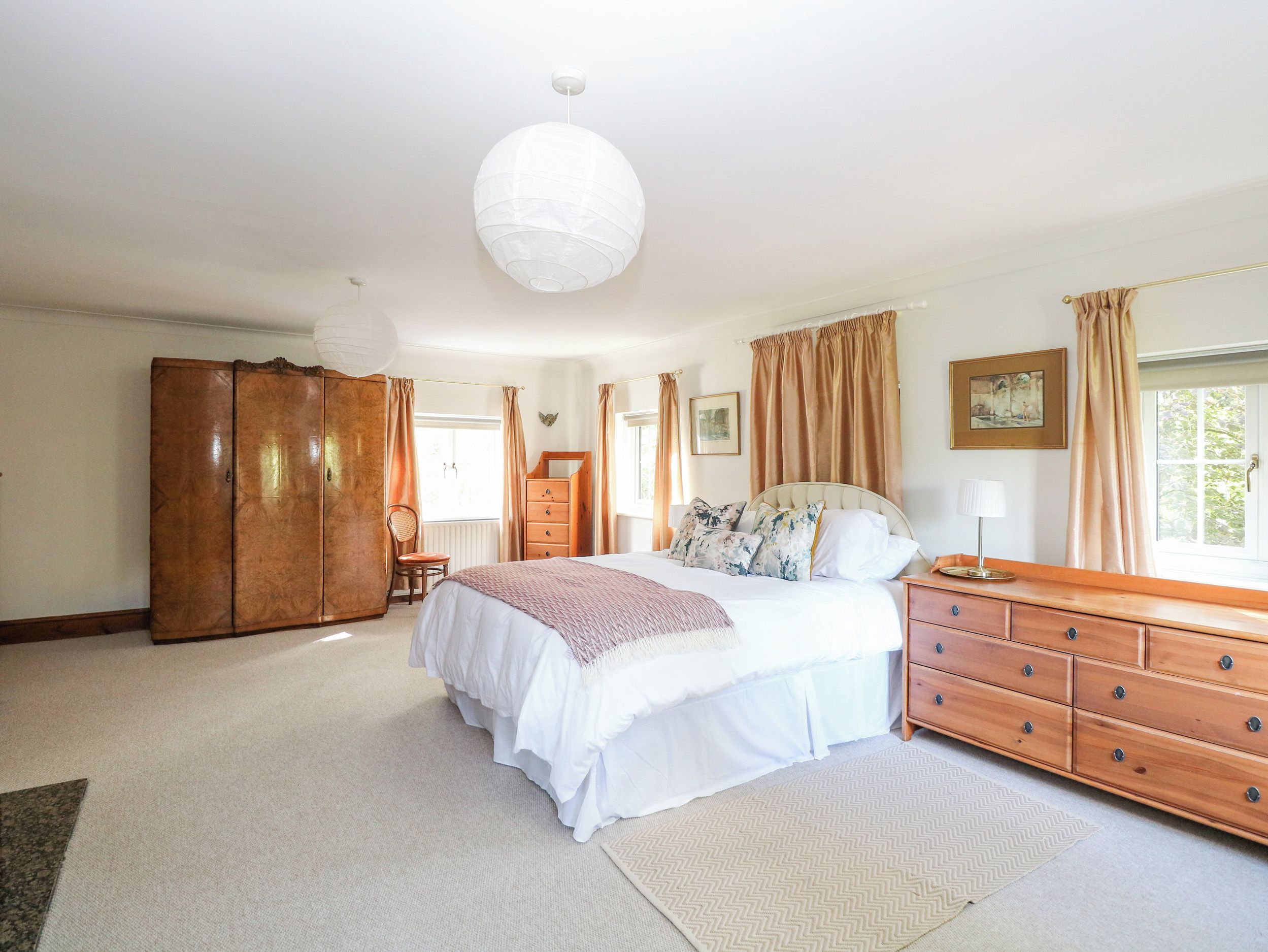 Un dormitorio amplio con una cama grande, un armario de madera y una lámpara colgante.