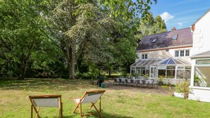 Ein Garten mit zwei Holzstühlen, einem Wintergarten und einem Haus mit Satteldach.