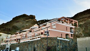 A multi-story hotel with balconies, a stone facade, and a mountainous backdrop. - Apartment with communal swimming pool in Playa de Mogan - Paraiso (lomo quiebre)
