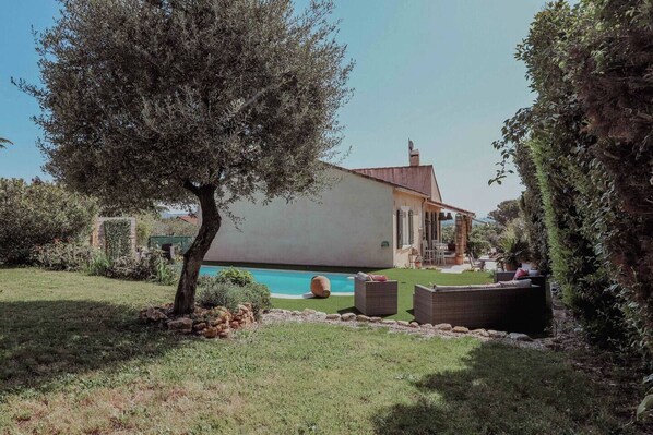 Une maison avec une piscine, entourée d’un jardin et d’un grand arbre.