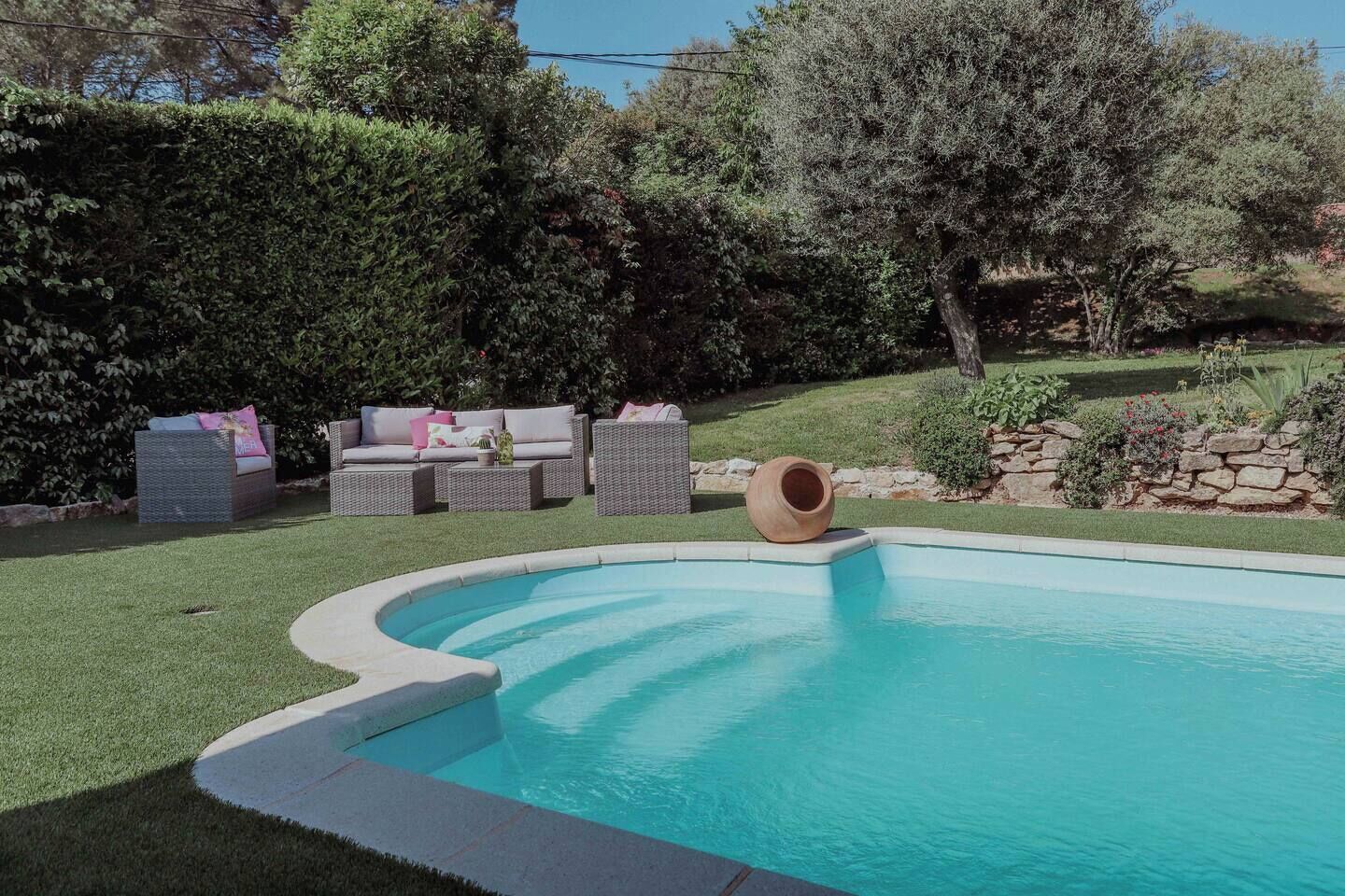 Une piscine à bord incurvé, entourée d’un mur de pierre et d’une zone herbeuse.