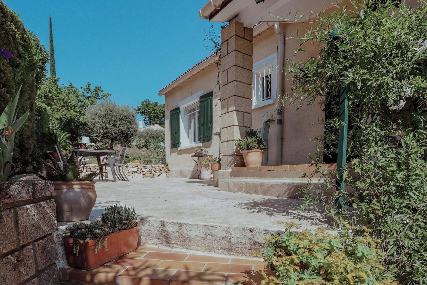 Een huis in mediterrane stijl, met een gevel van natuursteen, een klein terras met planten in potten en een tafel met stoelen.