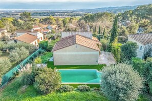 Une grande maison avec une piscine, entourée d’une végétation luxuriante et située dans un paysage vallonné.
