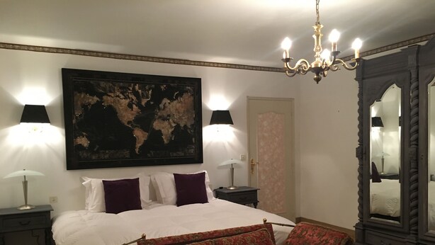 A bedroom with a large bed, two bedside tables with lamps, a world map on the wall, a red sofa, and a mirror with a decorative frame. - Le Belvedere (Thiviers)