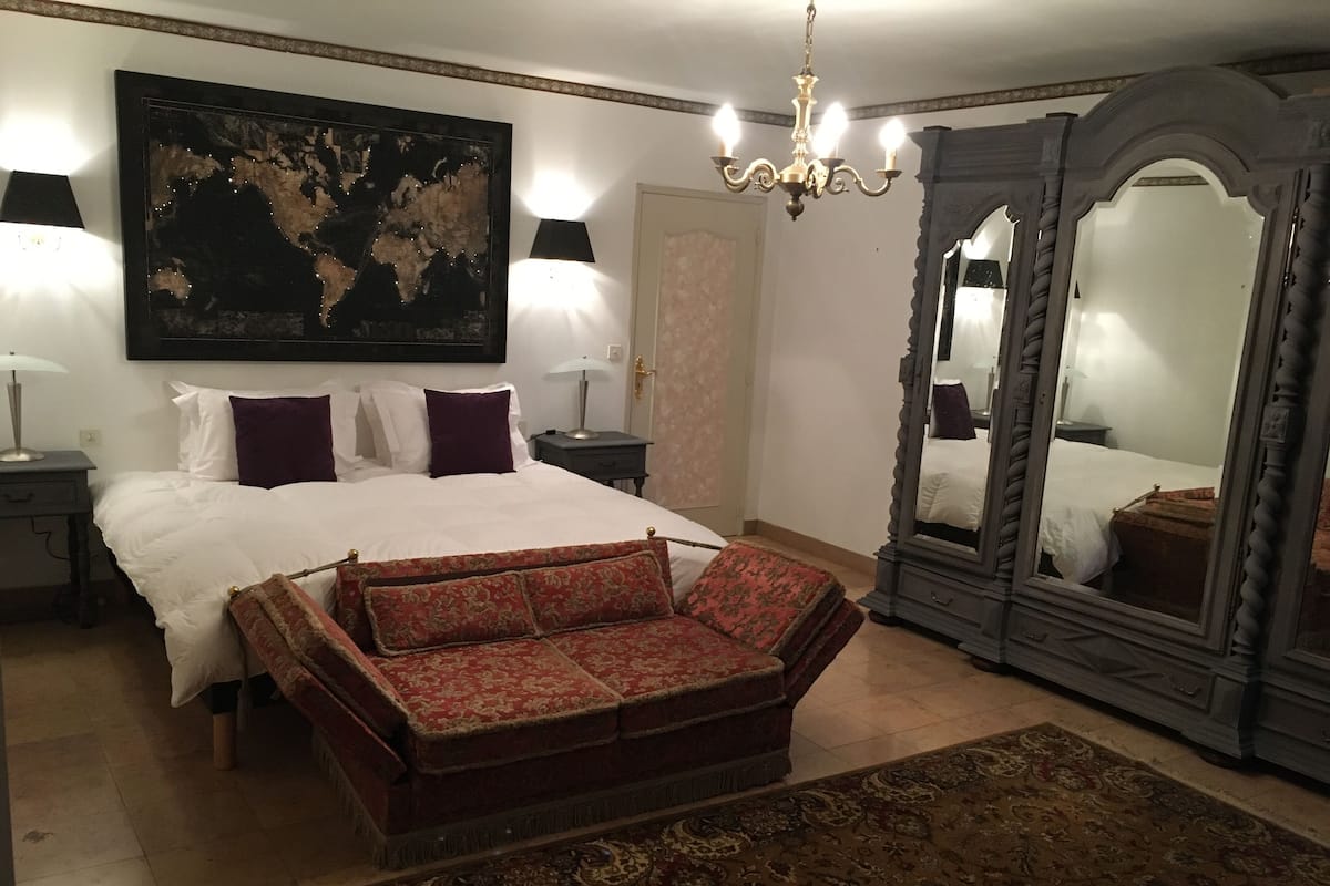Quarto com uma cama grande, duas mesas de cabeceira com luminárias, um espelho grande e um tapete decorativo.