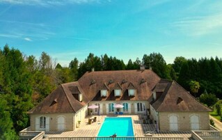 Una casa grande con piscina, rodeada de árboles y un cielo despejado.