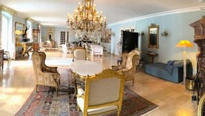 A spacious living room with a chandelier, a dining area with a round table, and a blue sofa. - Le Belvedere (Thiviers)