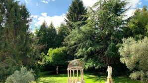 A gazebo surrounded by lush greenery and statues in a garden setting. - Le Belvedere (Thiviers)
