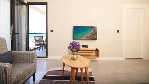 A modern living room with a sofa, a coffee table with a vase of flowers, a painting on the wall, and a sliding glass door leading to a balcony. - Krem Marin Suites (Cesme)