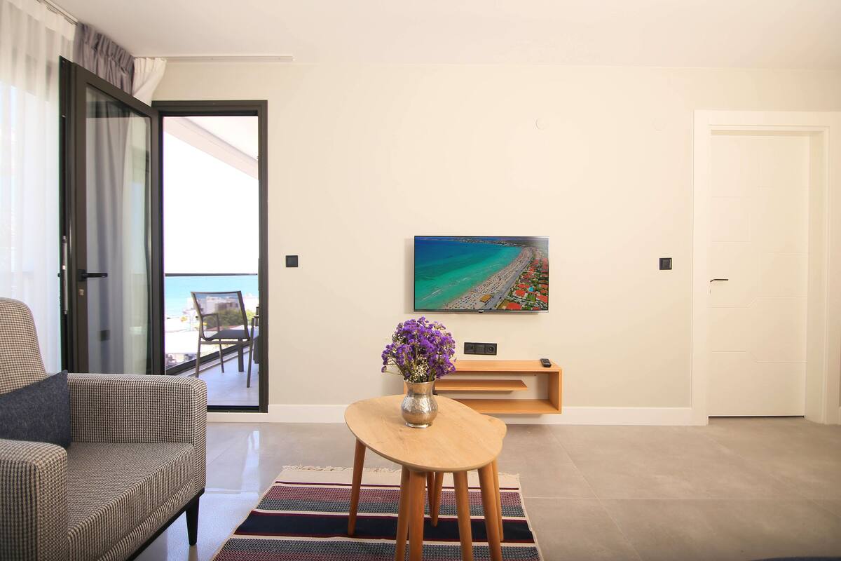 Un salon moderne avec un canapé, une table basse ornée d’un vase de fleurs, un tableau accroché au mur et une porte-fenêtre coulissante donnant sur un balcon.