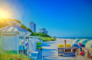 A beach scene with a small structure, possibly a gazebo, and a row of beach chairs. - FISHERMANS PARADISE  WATERFRONT POOL HOME 2 minute drive to the beach (naples)
