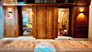 L’entrée d’un hôtel, avec une double porte en bois, une enseigne au-dessus indiquant « SANTA RITA RUTA » et une enseigne « HOSTAL » sur la gauche.