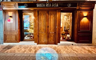 Entrada de un hotel con puertas de madera dobles, un cartel arriba que dice "SANTA RITA RUTA" y un letrero de "HOSTAL" a la izquierda.