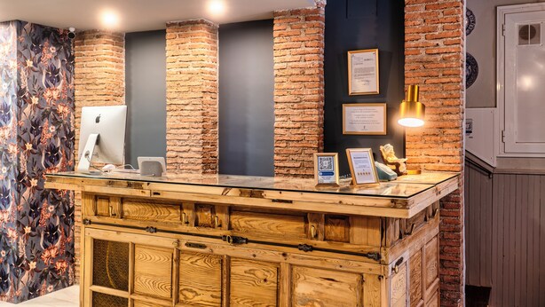 Un comptoir d’accueil avec un plateau en verre, des tiroirs en bois et un mur en briques en arrière-plan.