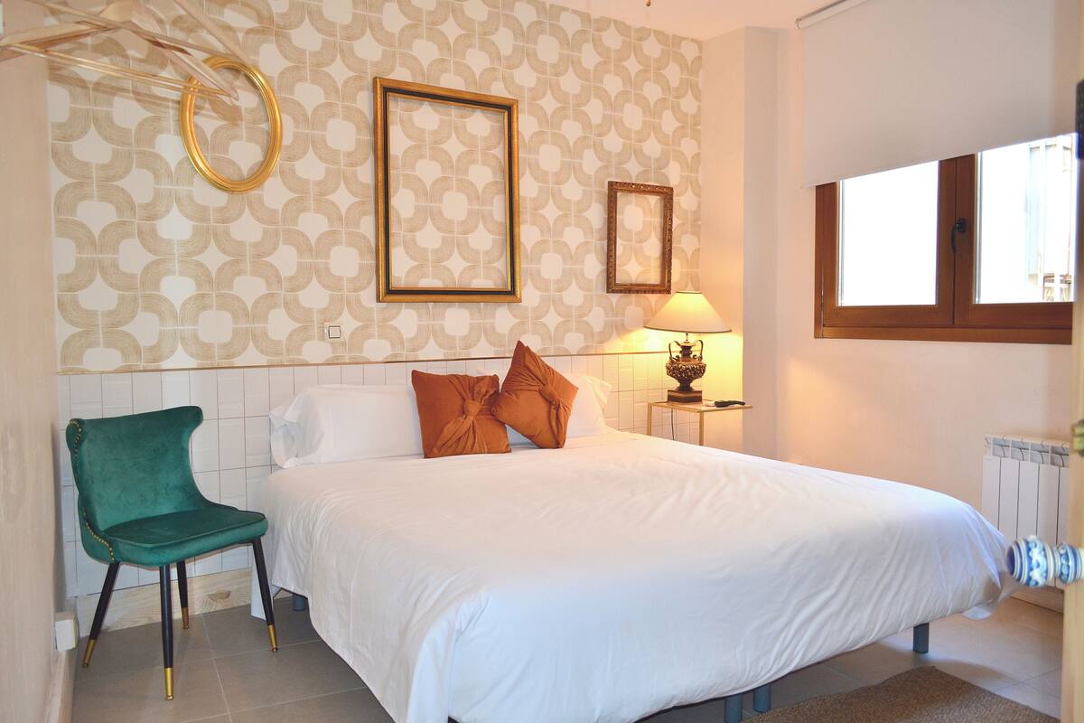 A bedroom with a bed, a chair, a lamp, and a window.
