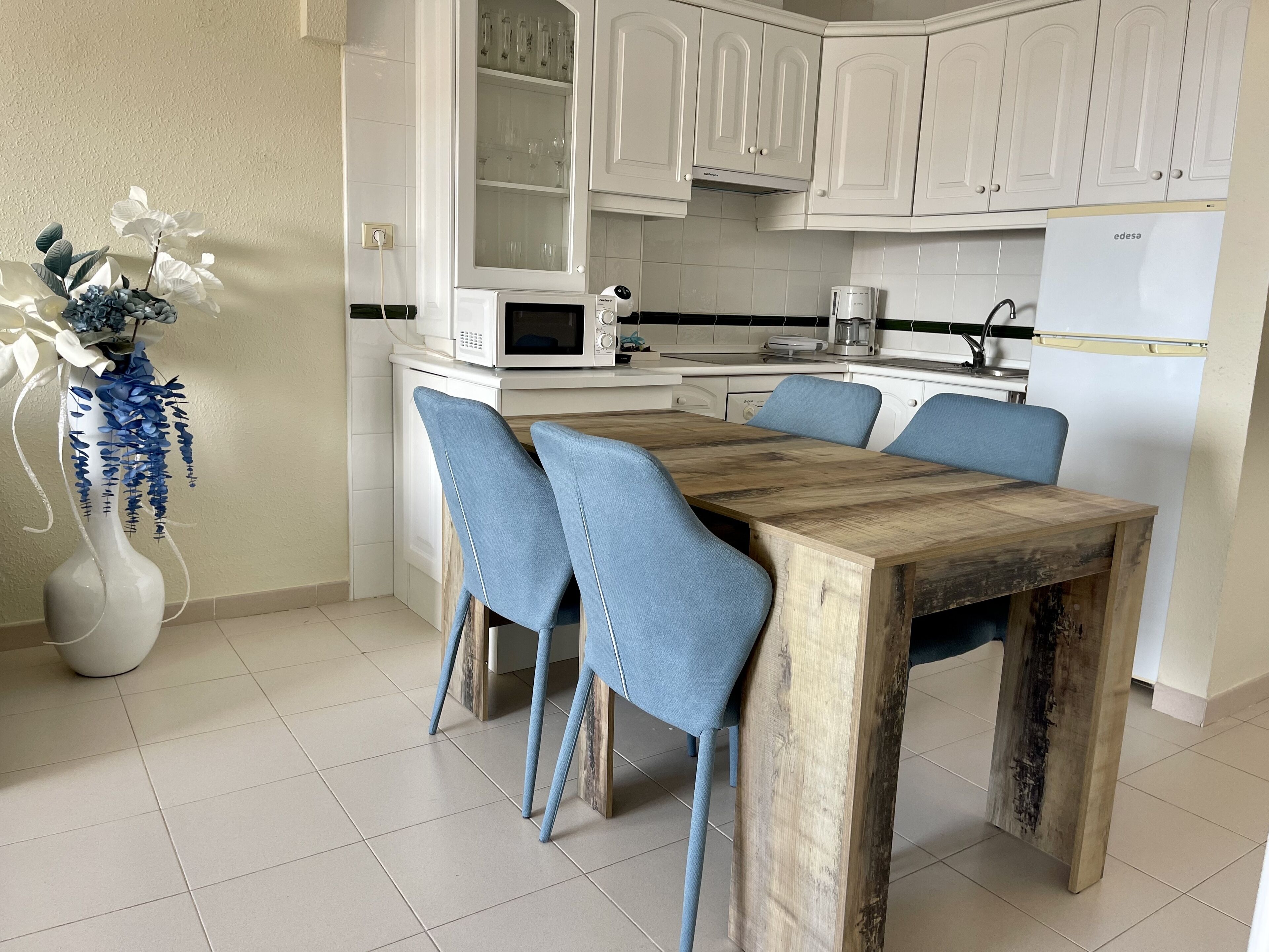 A modern kitchen with white cabinets, a wooden dining table, and blue chairs.