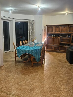 A dining area with a table set for four, surrounded by wooden chairs. There is a sliding glass door leading to an outdoor area.
