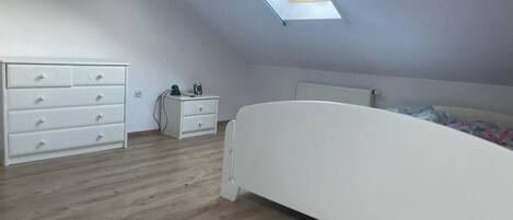 A bedroom with a skylight, a bed, a dresser, and a nightstand.
