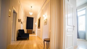 A hallway with wooden flooring, a dark-colored sofa, a small table, and framed pictures on the walls. - One Three One (Athens)