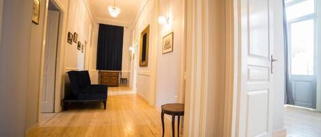 A hallway with wooden flooring, a dark-colored sofa, a small table, and framed pictures on the walls.