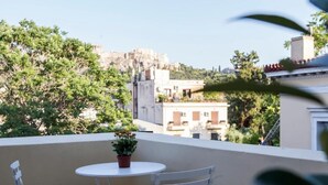 A balcony with a round table and two chairs, overlooking a cityscape with buildings and trees. - One Three One (Athens)