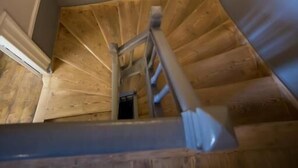 A wooden staircase with a handrail, a light fixture above, and a small vent on the wall. - One Three One (Athens)
