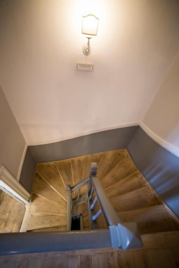 A wooden staircase with a handrail, a light fixture above, and a small vent on the wall.