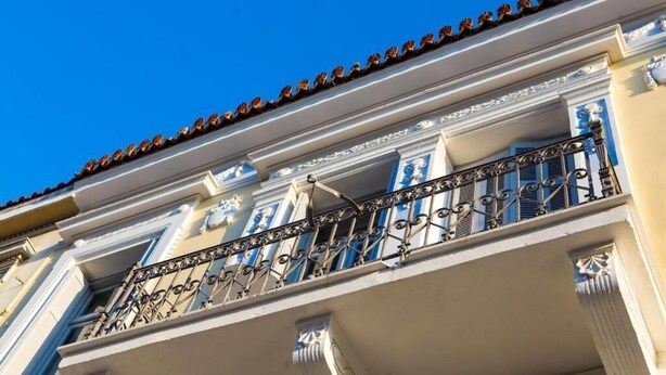 A building with a balcony featuring ornate metal railings and a tiled roof. - One Three One (Athens)