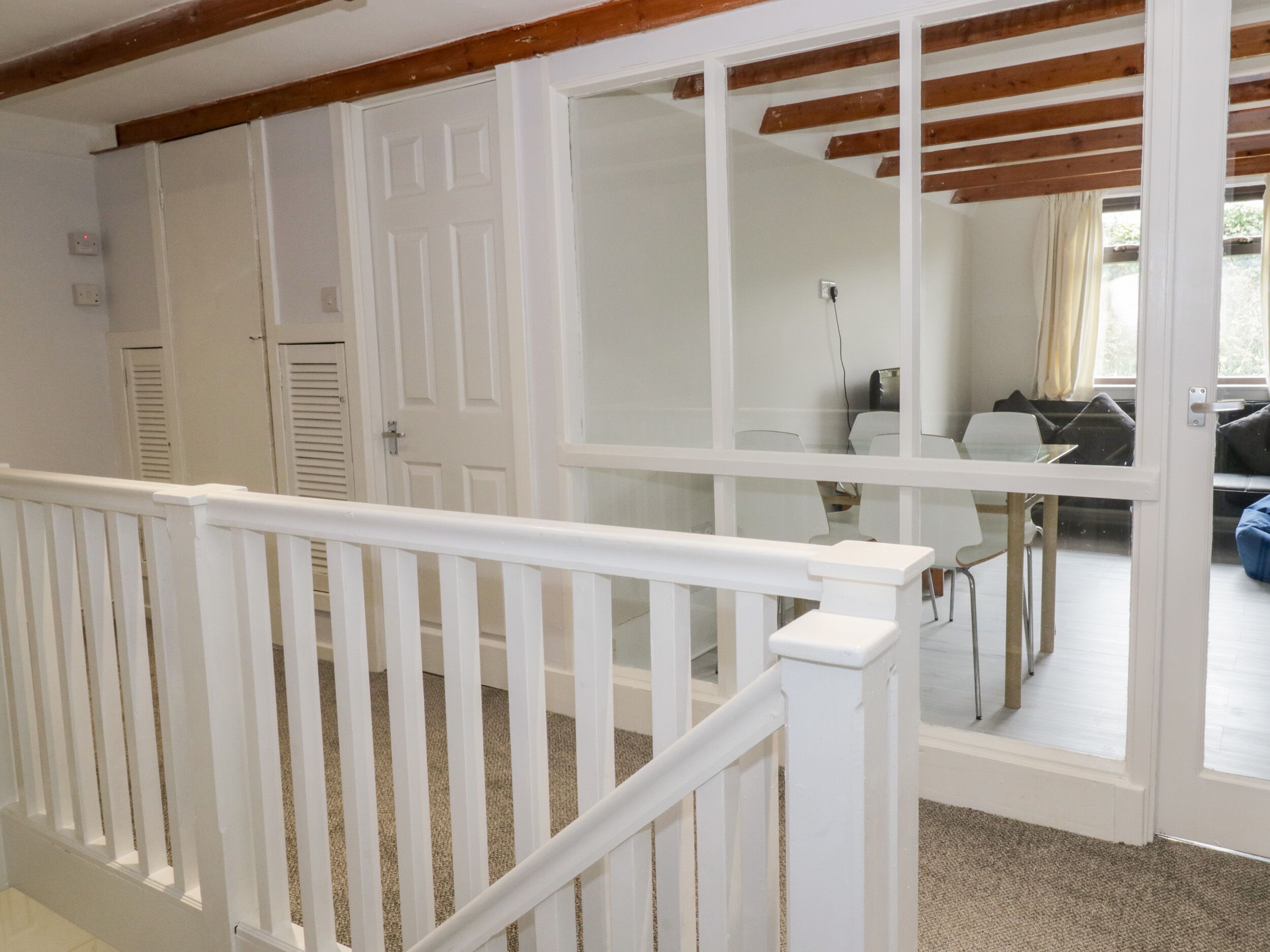 A room with a white door, a white railing, and a view of a dining area with chairs and a table.
