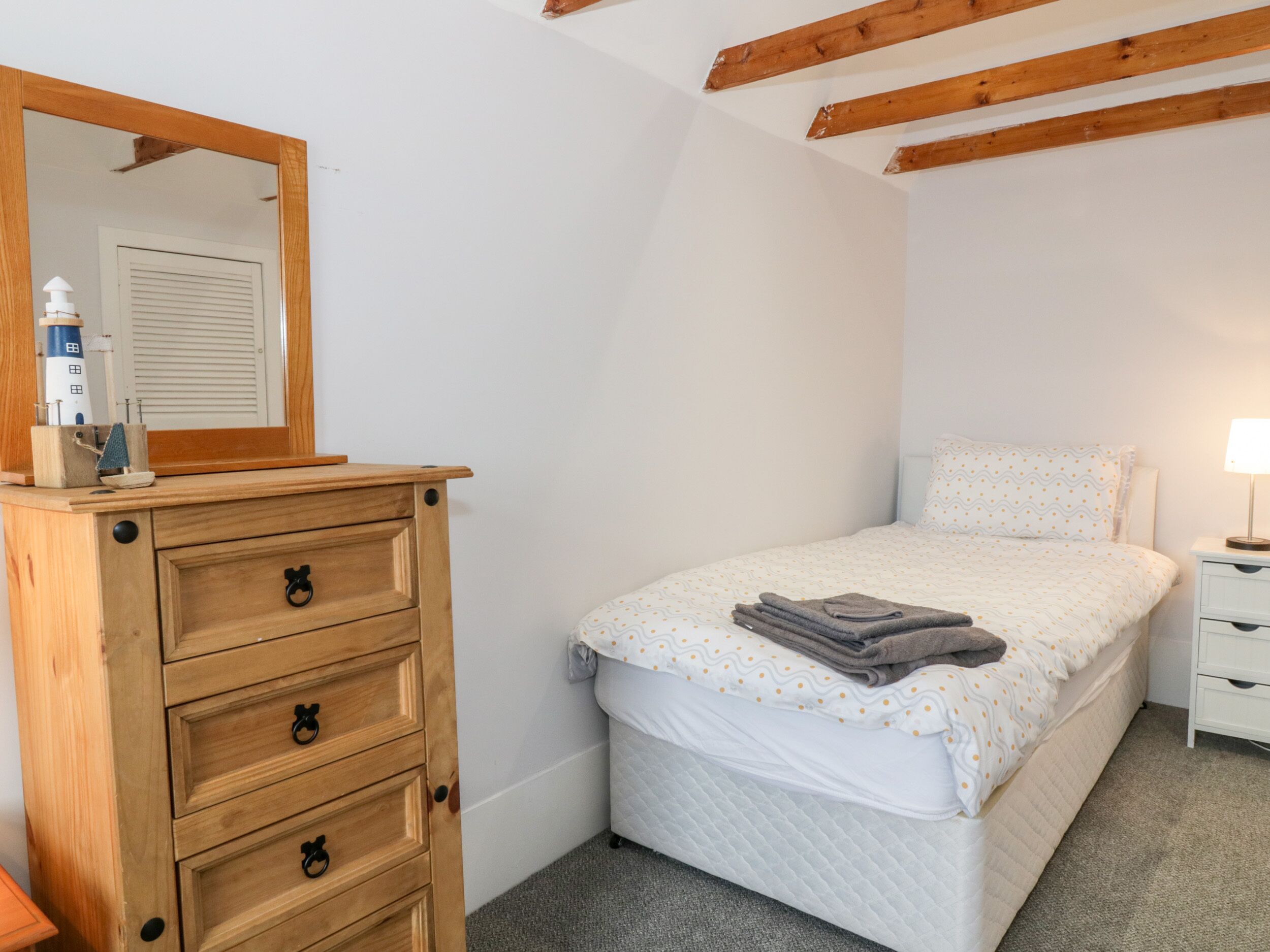 Um quarto com cômoda de madeira, cama com colchão acolchoado, abajur e espelho na parede.