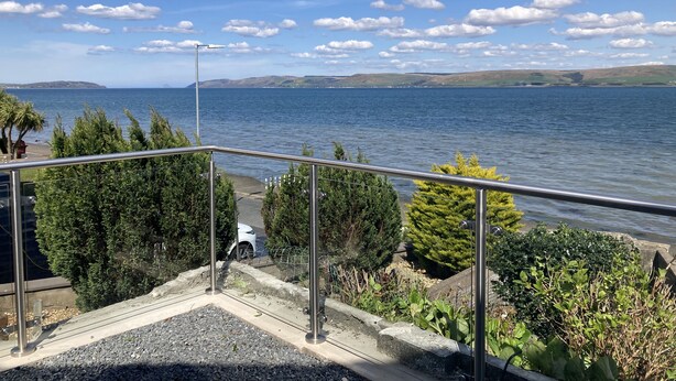 A balcony with a view of a lake, surrounded by greenery and a metal railing. - Waters Edge (Stranraer)